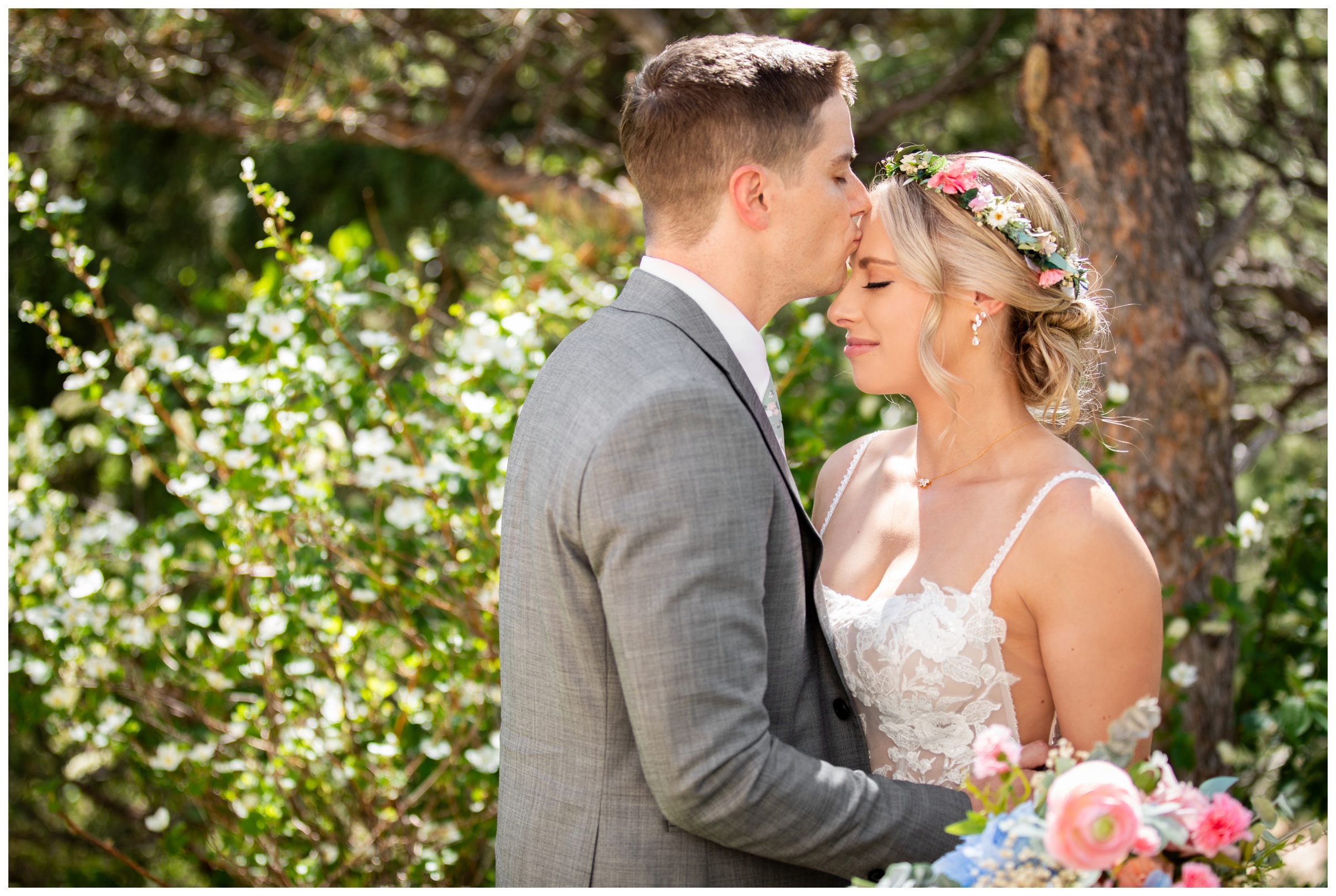 groom kissing bride's forehead under flowering trees during spring wedding at Lionscrest Manor