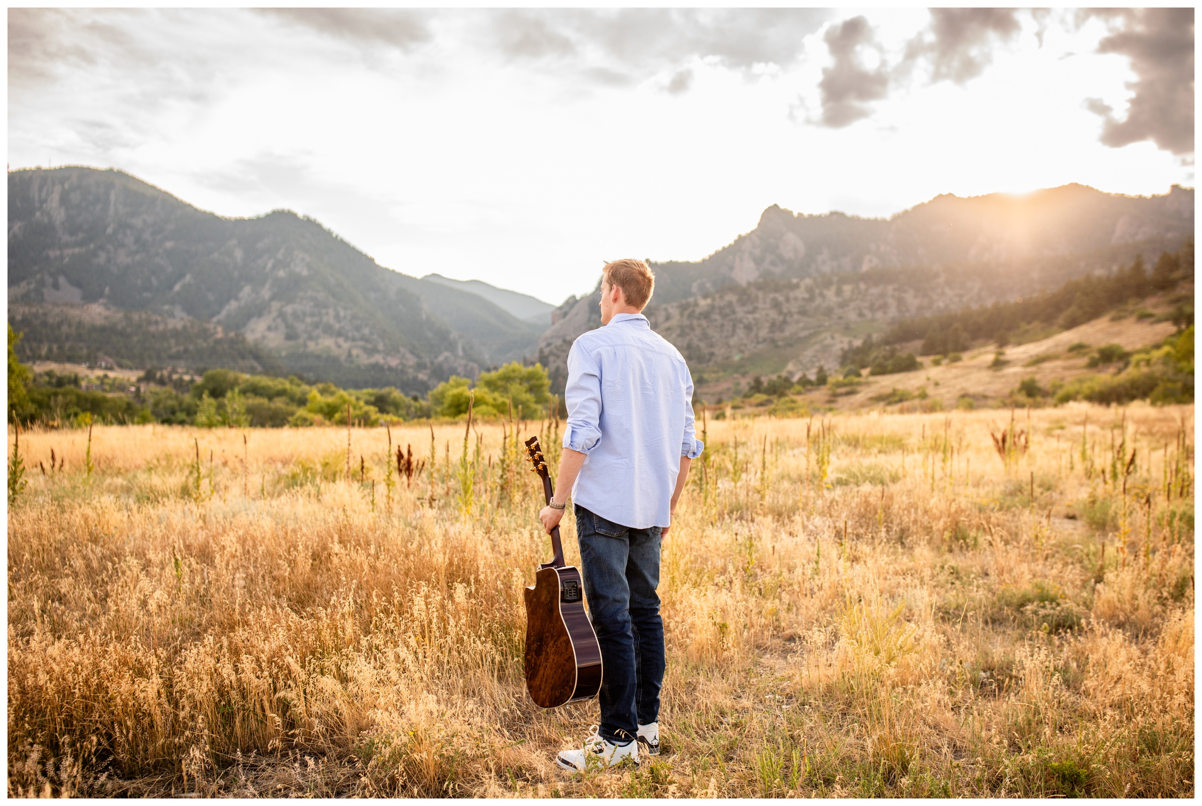 teen standing in a mountain field with his guitar during Boulder Colorado senior pictures at South Mesa Trail