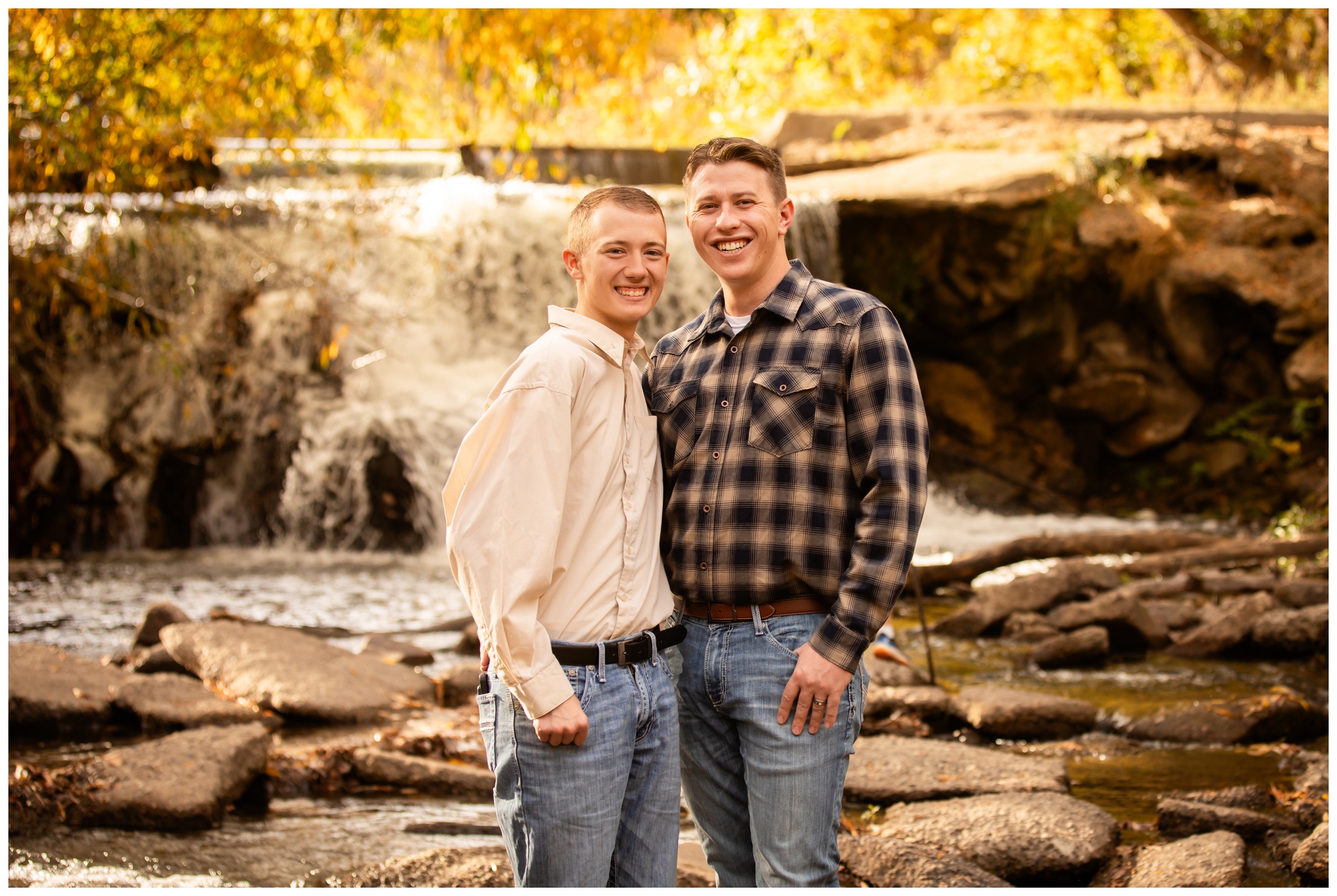 gay couple standing in front of waterfall at Golden Ponds in Longmont during fall photography session