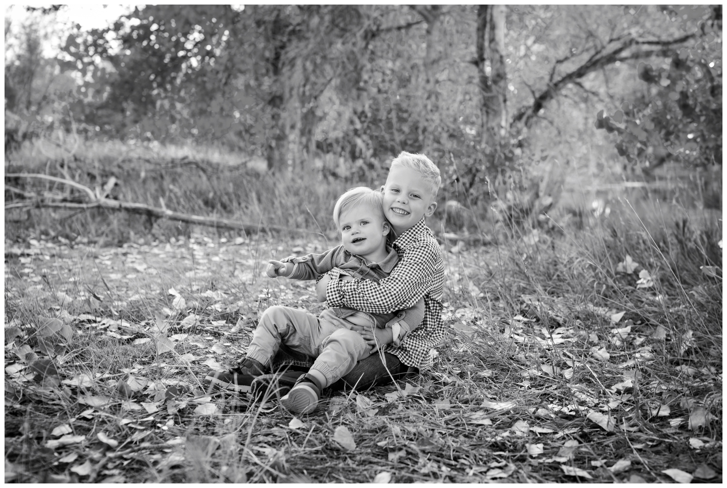 little boys sitting in the leaves during Longmont Colorado fall family pictures at Golden Ponds