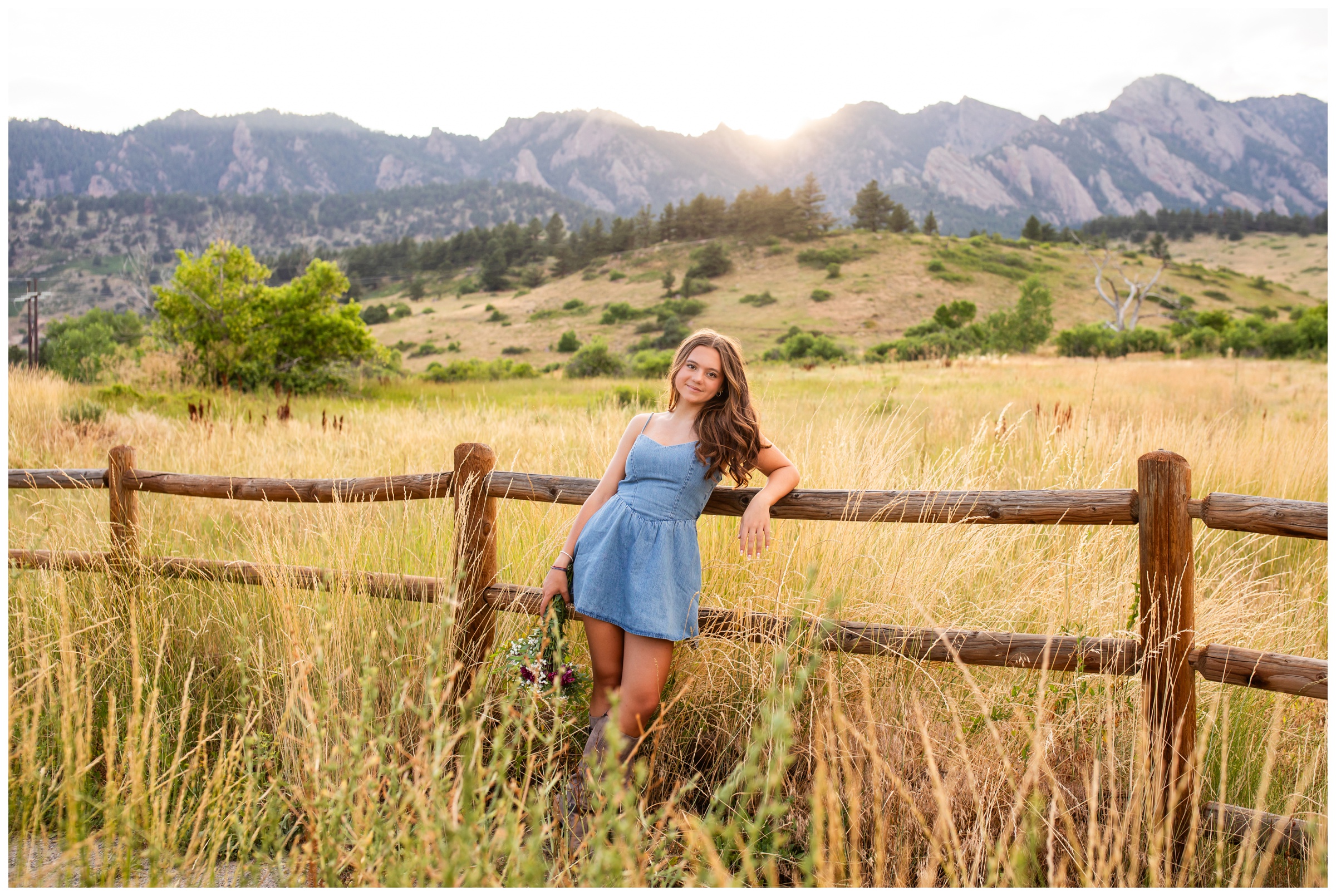 teen leaning against fence with flatiron mountains in background during Boulder Colorado high school senior pictures by Plum Pretty Photography