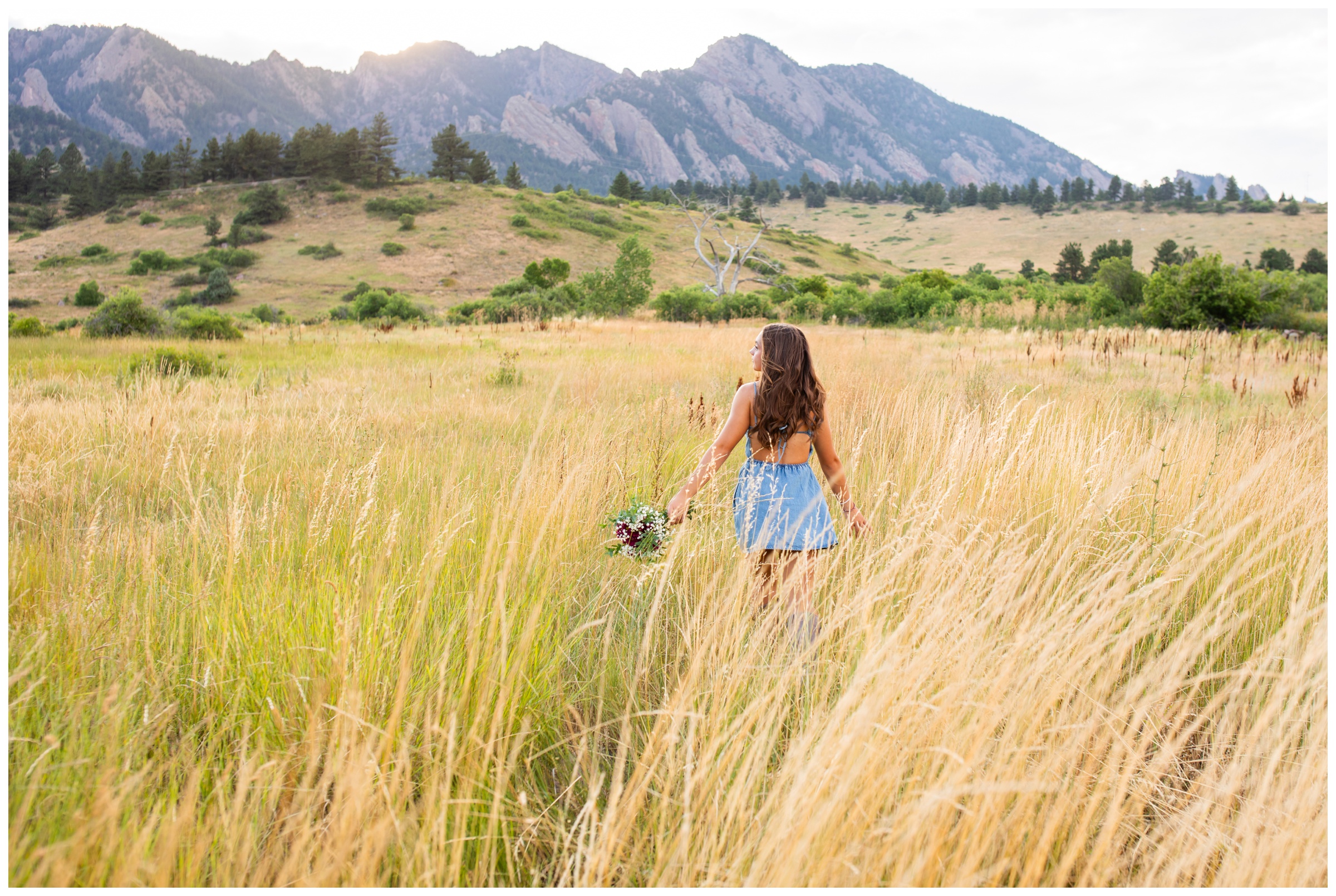teen walking through mountain field with bouquet during unique senior photos in Boulder Colorado