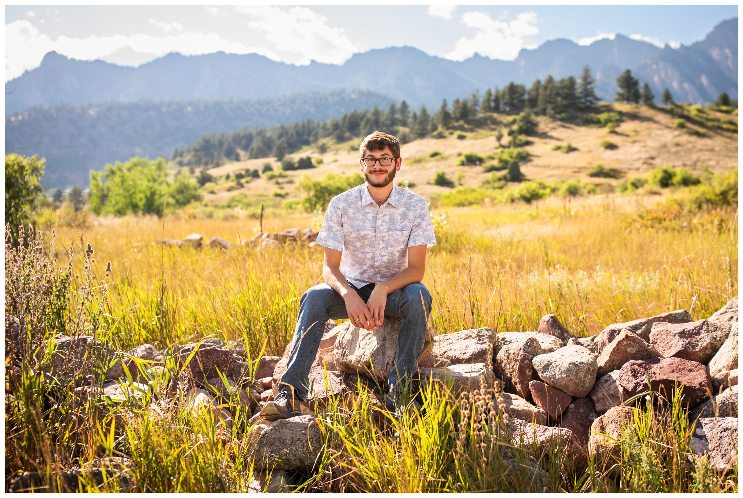 teen guy sitting on rock pile with mountains in background during Boulder senior portraits 