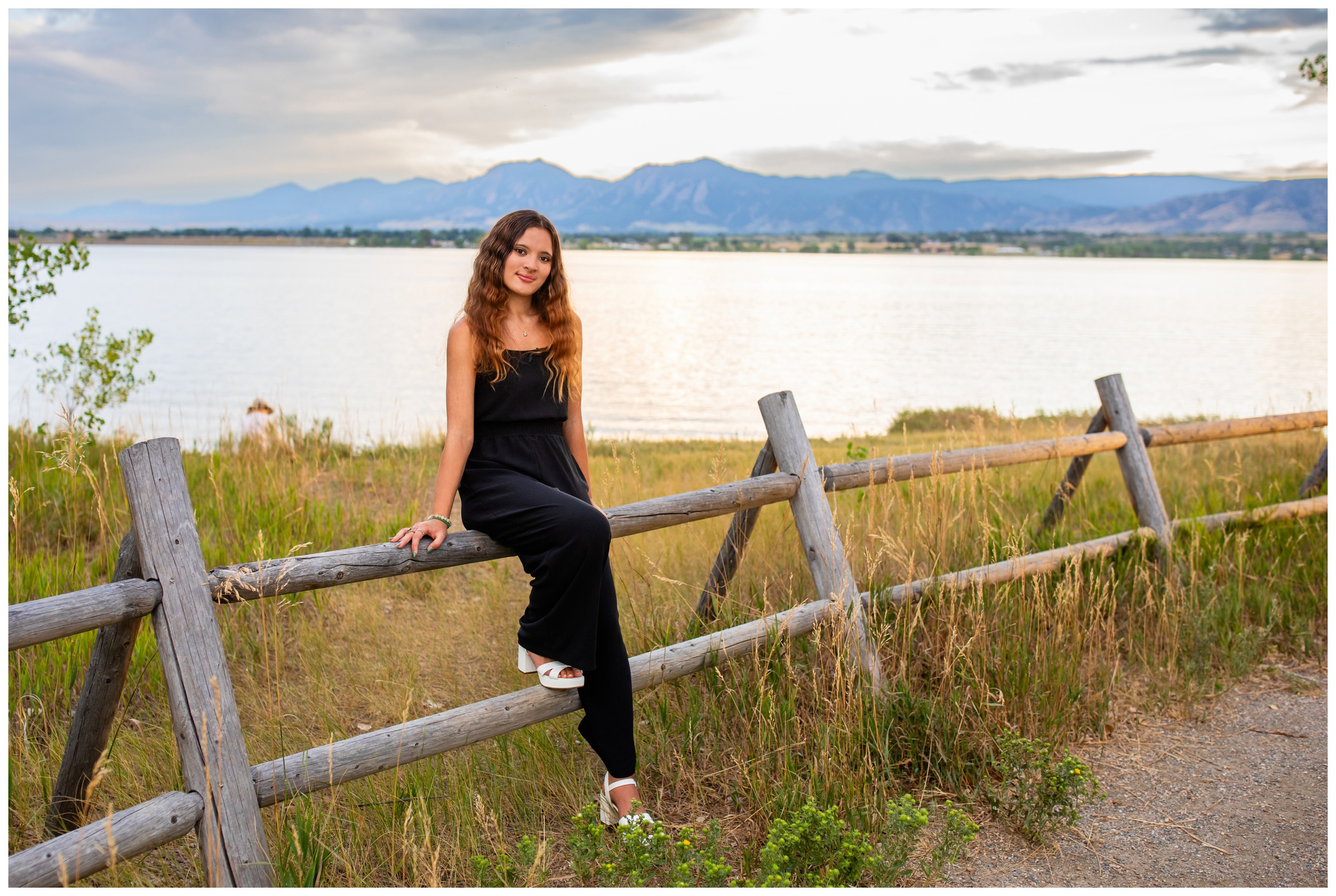 teen sitting on fence with flatirons mountains in background during Silver Creek High School senior pictures 