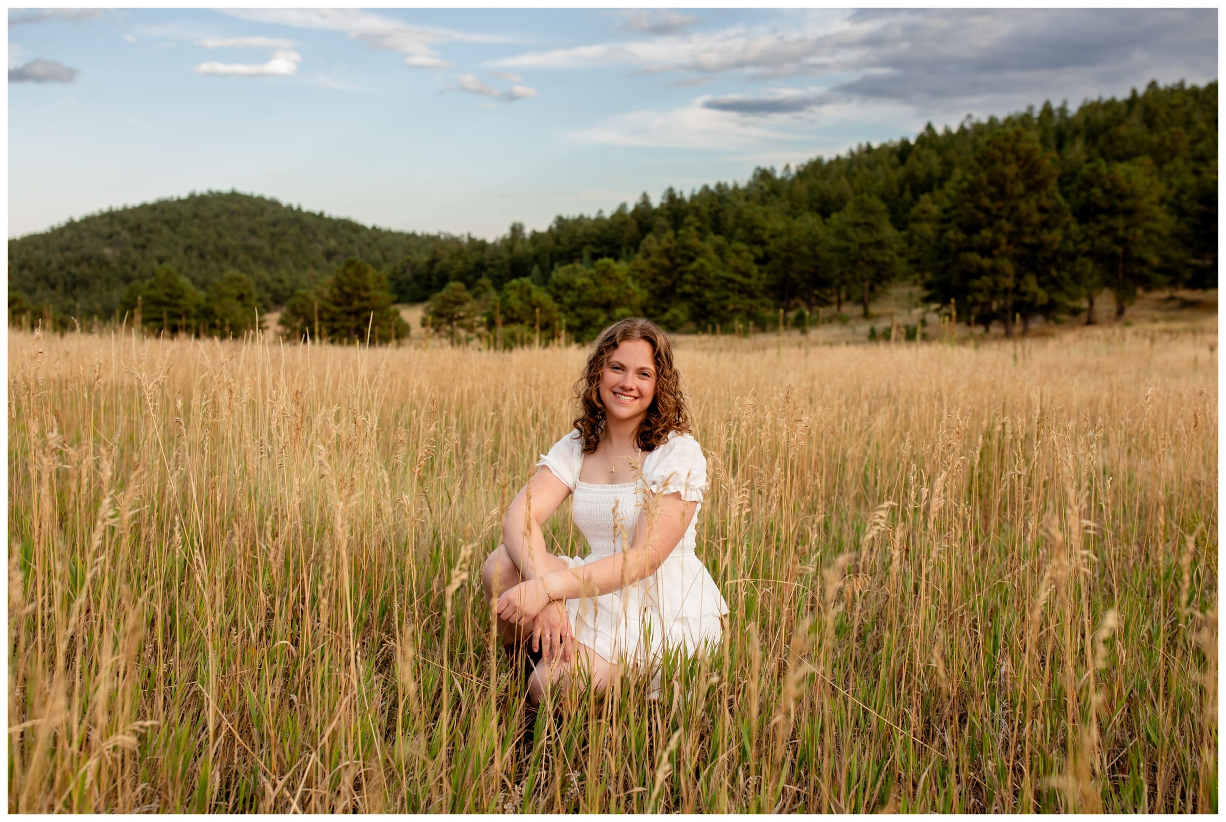 teen squatting in mountain field during high school graduation photography session 