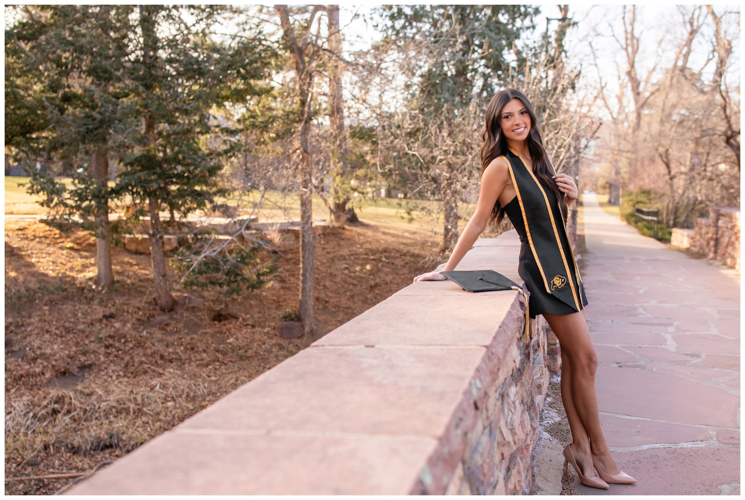 woman leaning on bridge during Colorado college cap and gown photo session by Plum Pretty Photography