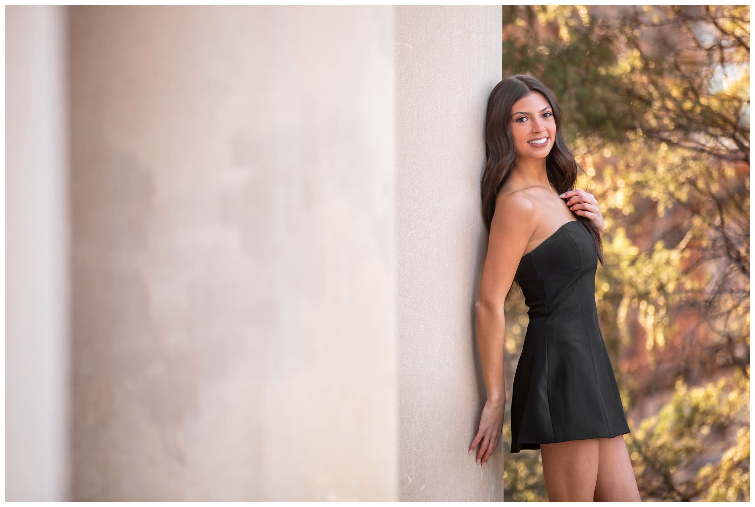 woman leaning on column at CU Boulder during college cap and gown senior photos in Boulder